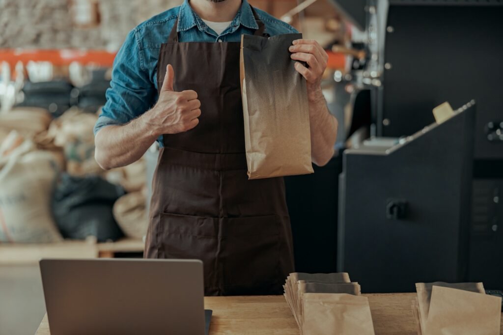 Close up of business owner hands holding roasted coffee beans in paper bag in coffee factory